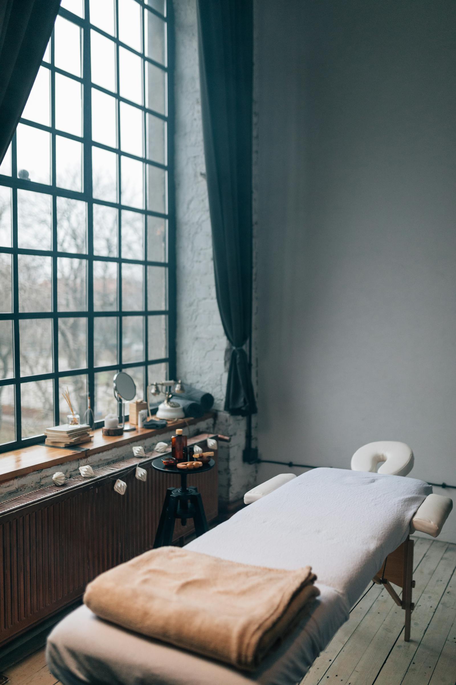 A calm, dimly lit massage treatment room with a draped window