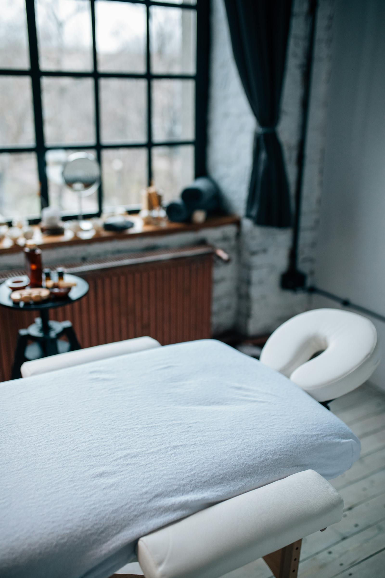 Loft treatment room with a tall draped window and warm linens